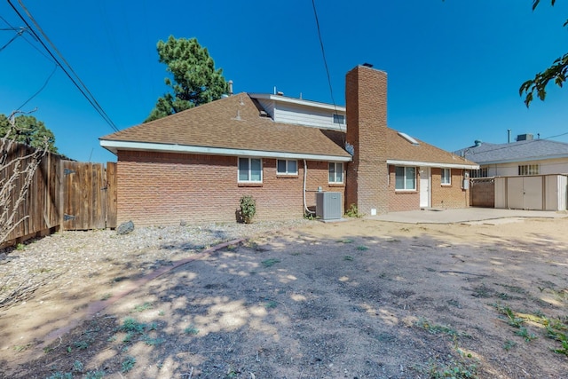 back of property featuring brick siding, a chimney, fence, and central air condition unit