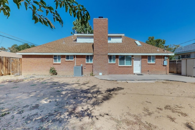 rear view of property featuring a chimney, fence, central AC, and brick siding