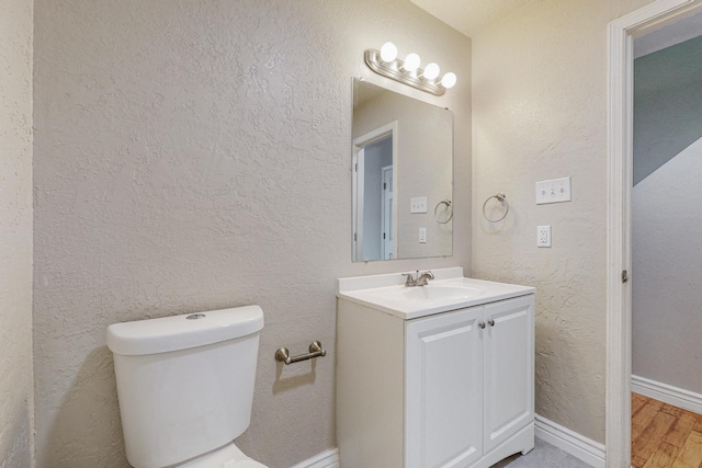 half bathroom featuring baseboards, a textured wall, toilet, wood finished floors, and vanity