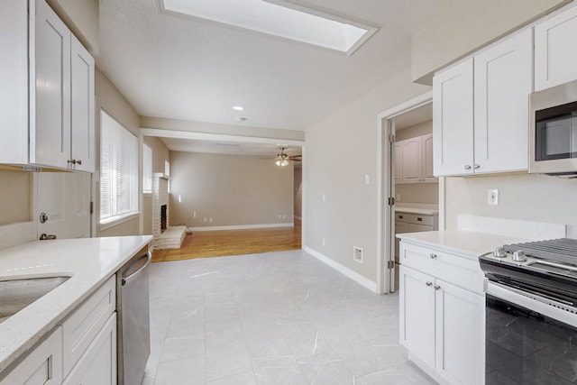 kitchen featuring a skylight, appliances with stainless steel finishes, white cabinets, and a ceiling fan