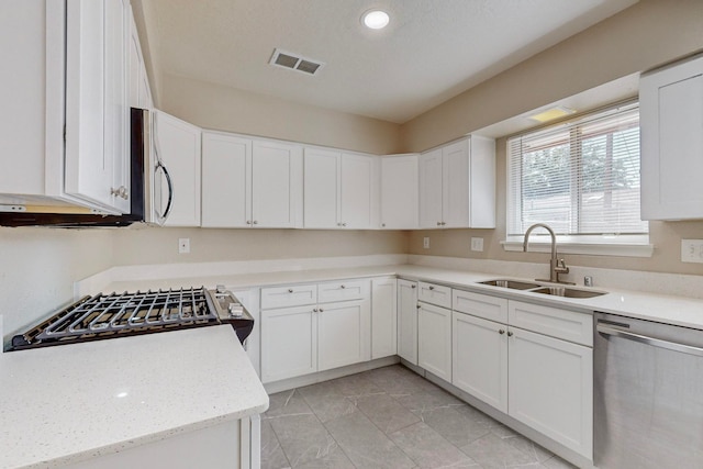 kitchen with white cabinets, appliances with stainless steel finishes, sink, and light stone countertops