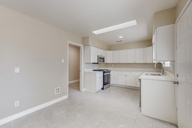 kitchen featuring stainless steel appliances, a skylight, a sink, baseboards, and light countertops