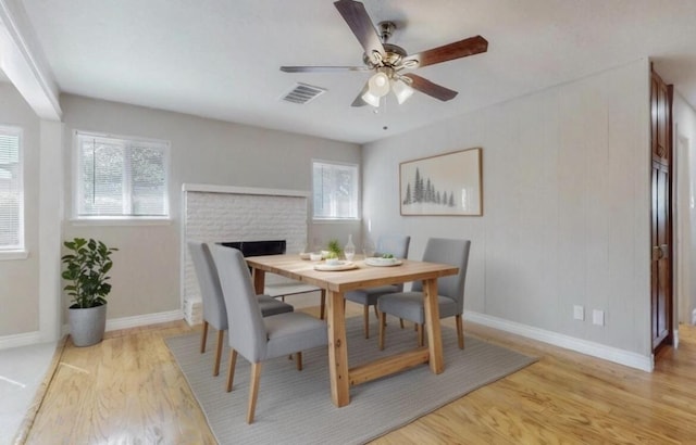 dining space featuring light wood finished floors, baseboards, visible vents, ceiling fan, and a fireplace