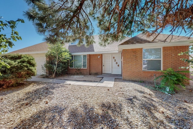 ranch-style home with brick siding, an attached garage, and a shingled roof