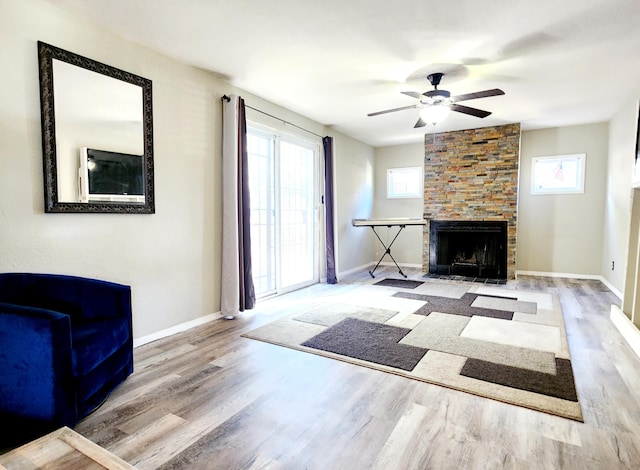 living room featuring ceiling fan, a stone fireplace, and light hardwood / wood-style flooring