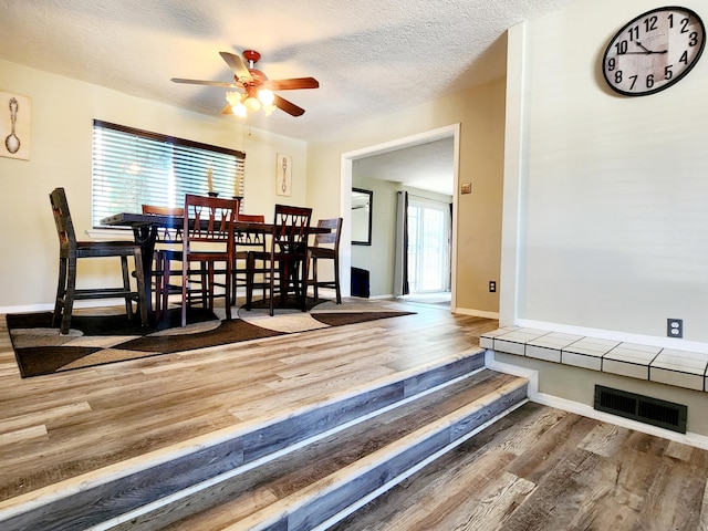 dining area featuring ceiling fan, wood-type flooring, and a textured ceiling