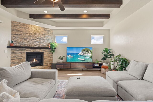 living room featuring ceiling fan, beam ceiling, a stone fireplace, and light hardwood / wood-style floors