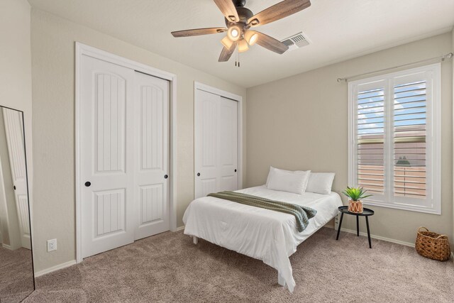 bedroom with ceiling fan, light colored carpet, and two closets