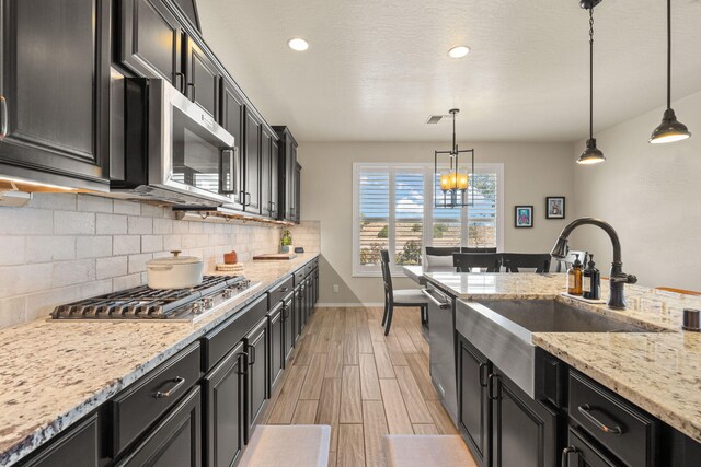 kitchen with light stone countertops, sink, light hardwood / wood-style flooring, appliances with stainless steel finishes, and decorative light fixtures