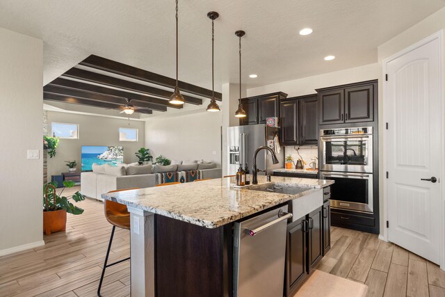 kitchen featuring a center island with sink, beam ceiling, appliances with stainless steel finishes, and light hardwood / wood-style flooring