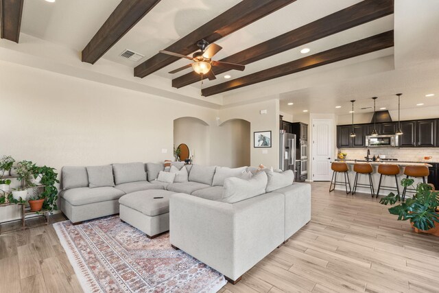 living room with ceiling fan, beamed ceiling, and light wood-type flooring