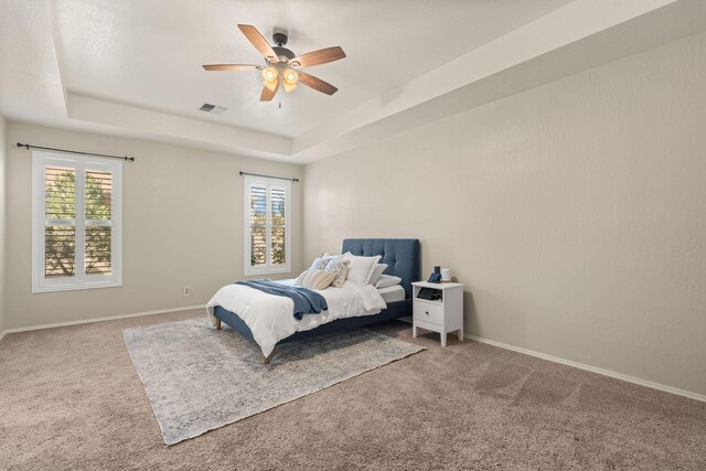 carpeted bedroom featuring ceiling fan, a raised ceiling, and multiple windows