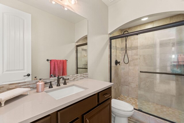 bathroom featuring vanity, a shower with door, toilet, and backsplash