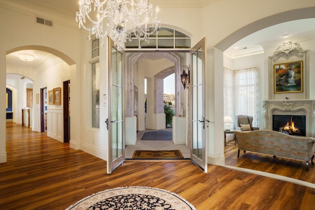 hall featuring french doors, an inviting chandelier, wood-type flooring, and ornamental molding