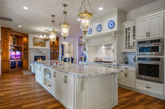 kitchen featuring white cabinets, backsplash, a center island with sink, and hanging light fixtures