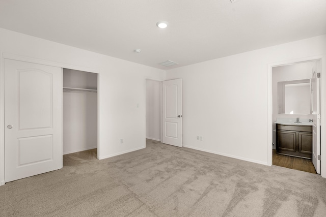 unfurnished bedroom featuring a closet, ensuite bath, sink, and light carpet