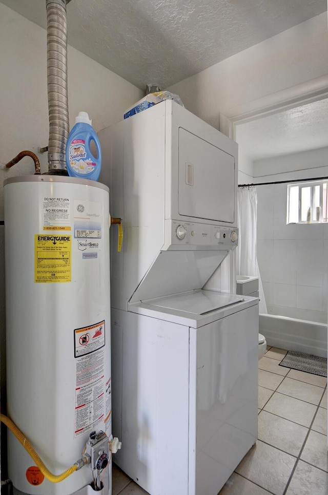 clothes washing area with stacked washer / drying machine, water heater, light tile patterned flooring, and a textured ceiling