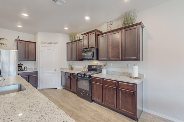 kitchen featuring sink, light stone counters, dark brown cabinetry, black appliances, and light wood-type flooring