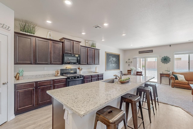 kitchen with a kitchen breakfast bar, sink, a center island with sink, and range with gas cooktop