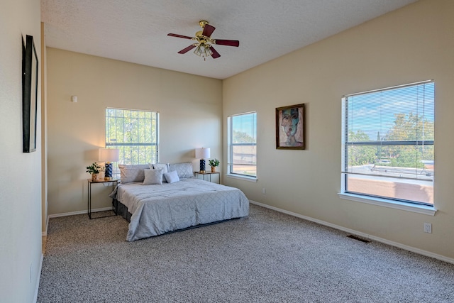 carpeted bedroom with a textured ceiling, multiple windows, and ceiling fan