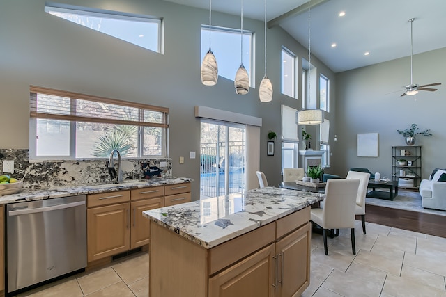 kitchen featuring ceiling fan, dishwasher, a center island, a high ceiling, and light stone counters