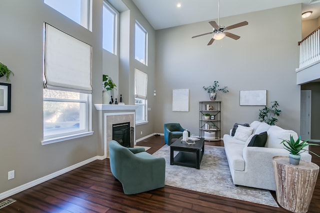 living room featuring a tile fireplace, a towering ceiling, dark hardwood / wood-style flooring, and ceiling fan