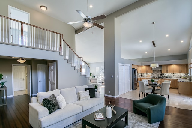 living room featuring ceiling fan, sink, a towering ceiling, and light hardwood / wood-style floors