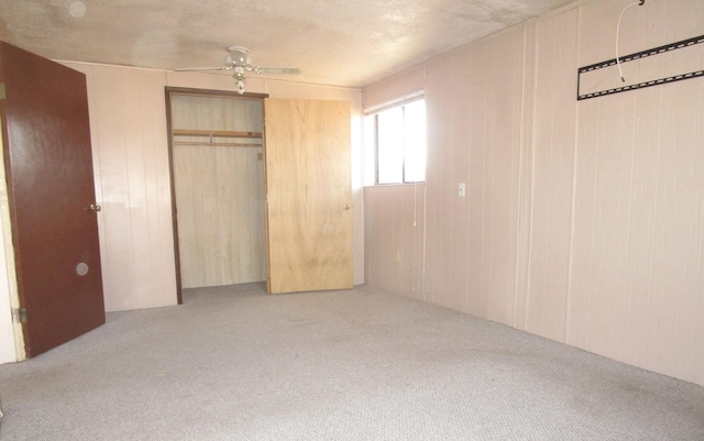 unfurnished bedroom featuring a closet, ceiling fan, light colored carpet, and wood walls