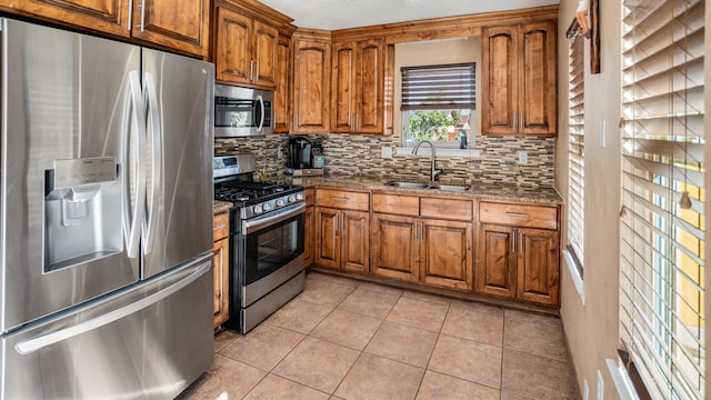 kitchen featuring appliances with stainless steel finishes, dark stone countertops, sink, and light tile patterned floors