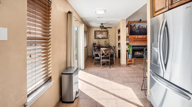 kitchen featuring ceiling fan, stainless steel refrigerator with ice dispenser, a fireplace, and light tile patterned floors