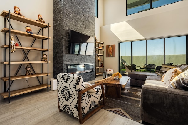 living room featuring light hardwood / wood-style flooring, a stone fireplace, and a towering ceiling