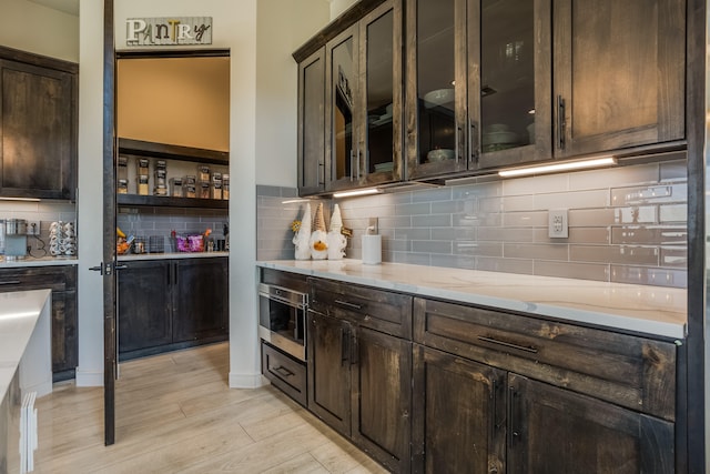 bar with light hardwood / wood-style flooring, decorative backsplash, dark brown cabinetry, and light stone counters