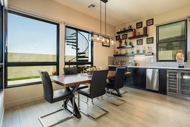 dining room featuring wine cooler, bar, and light hardwood / wood-style flooring