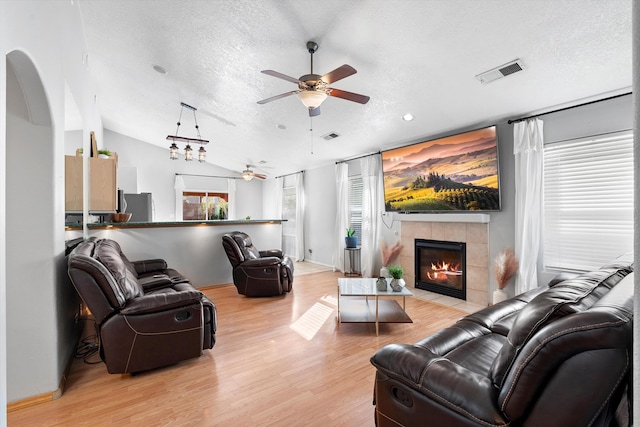 living room featuring light wood-type flooring, vaulted ceiling, a tile fireplace, and a textured ceiling