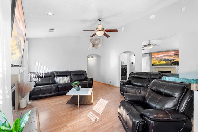 living room with ceiling fan, washer / dryer, a tiled fireplace, a textured ceiling, and light hardwood / wood-style floors