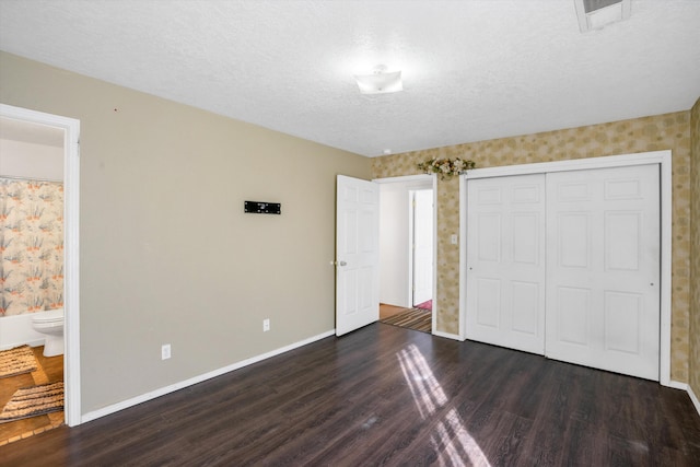 unfurnished bedroom with ensuite bath, a closet, dark wood-type flooring, and a textured ceiling