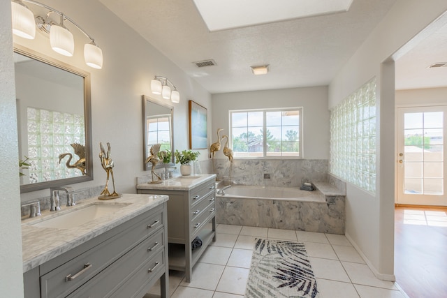 bathroom featuring tile patterned flooring, tiled tub, vanity, and a textured ceiling