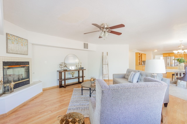 living room with ceiling fan with notable chandelier, a fireplace, and light hardwood / wood-style floors