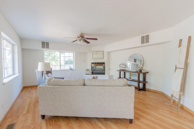 living room with ceiling fan, a tile fireplace, light wood-type flooring, and a healthy amount of sunlight