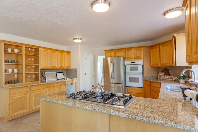 kitchen featuring sink, kitchen peninsula, appliances with stainless steel finishes, light tile patterned floors, and backsplash