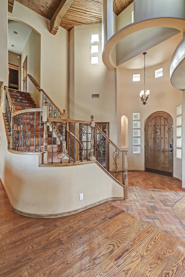 foyer featuring a notable chandelier, a healthy amount of sunlight, a towering ceiling, and wood ceiling