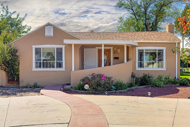 bungalow-style home with a chimney, roof with shingles, and stucco siding