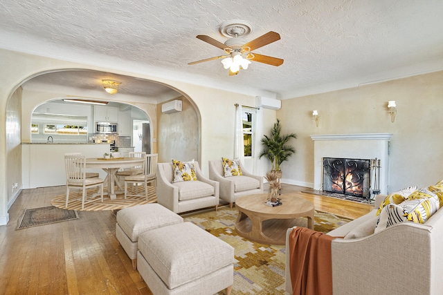 living room with hardwood / wood-style floors, ceiling fan, an AC wall unit, and a textured ceiling