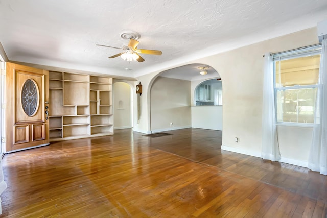 unfurnished living room with hardwood / wood-style floors, baseboards, arched walkways, and ceiling fan