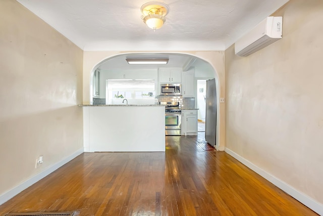 interior space with visible vents, baseboards, a wall mounted AC, arched walkways, and dark wood-type flooring