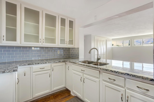 kitchen with light stone counters, backsplash, white cabinetry, and a sink