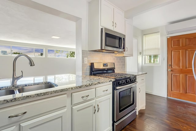 kitchen with a wall mounted air conditioner, light stone counters, stainless steel appliances, white cabinets, and dark hardwood / wood-style floors