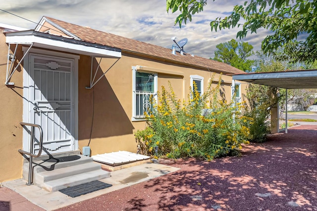 doorway to property featuring stucco siding and a shingled roof