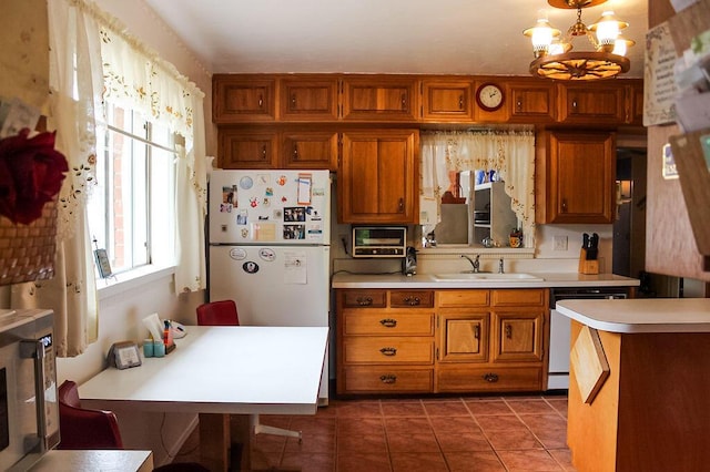 kitchen with sink, dark tile patterned flooring, white refrigerator, stainless steel dishwasher, and a notable chandelier