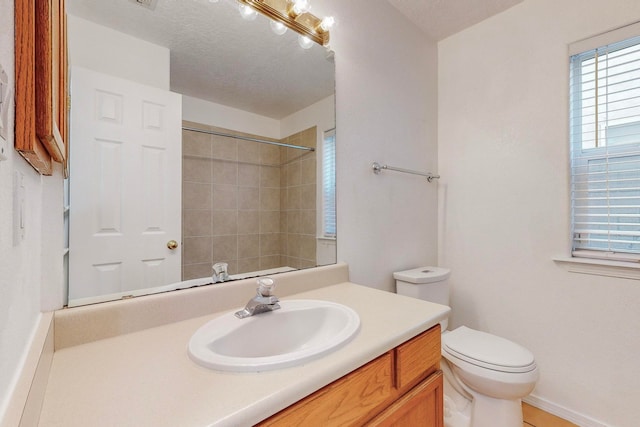 bathroom with toilet, a textured ceiling, vanity, and tiled shower